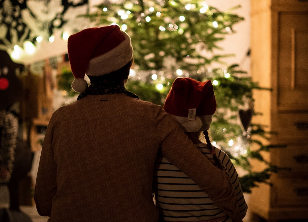 A rea view of a parent sat with a child in front of a lit up Christmas tree.