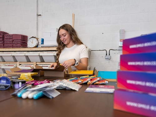 A women putting items into a box stood at a table.