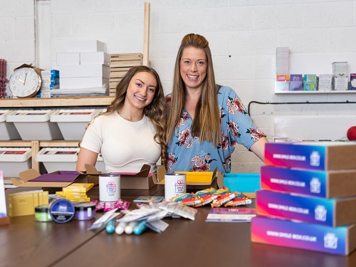 Two women standing behind a table with boxes on the table in front of them