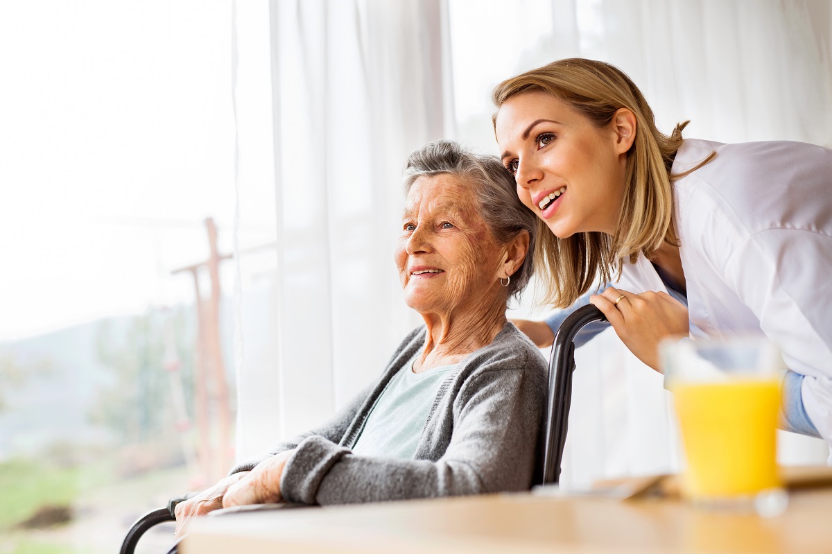 Older person in a chair with a younger person leaning over their shoulder smiling