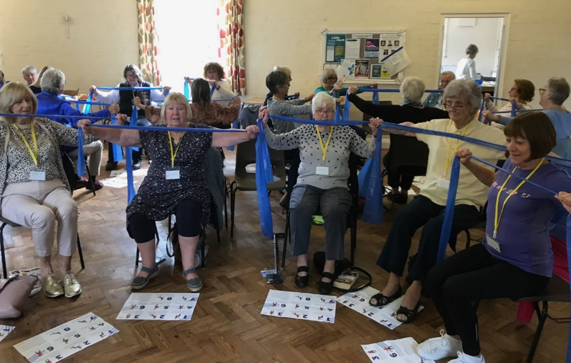 Corn dollies in a resistance bands session exercising their arms whilst sat on chairs