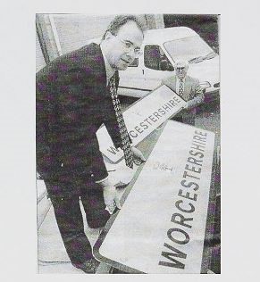 A black and white photo of two people unloading road signs that say Worcestershire. 