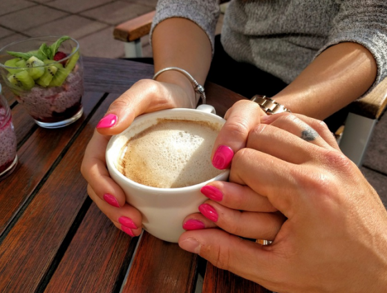 People holding hands over a cup of coffee in a supportive way