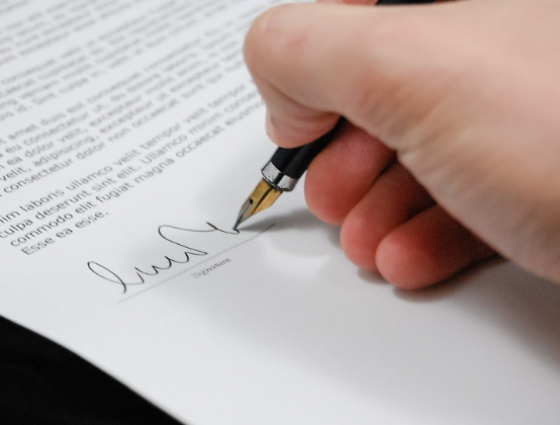 Hand holding a pen signing a name on a document
