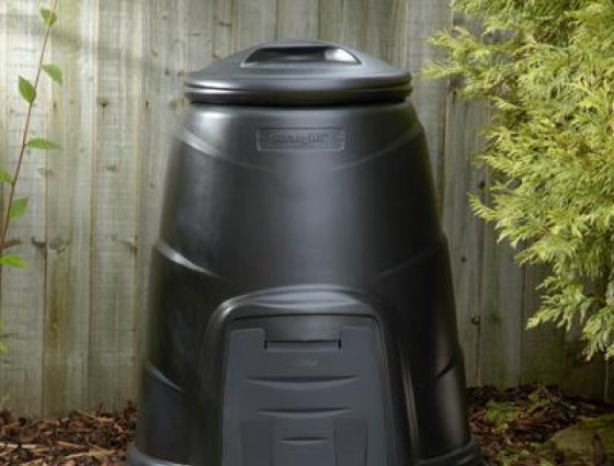 A black compost bin stood by a fence.