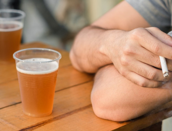 Close up of a hand with a cigarette and a beer on the table