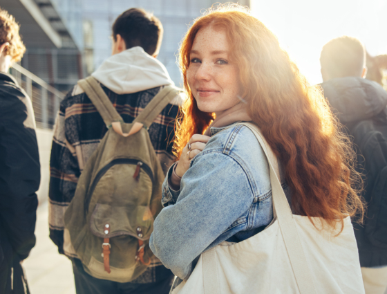 Landscape image of 4 students walking. A girl with long red hair is looking back to the camera