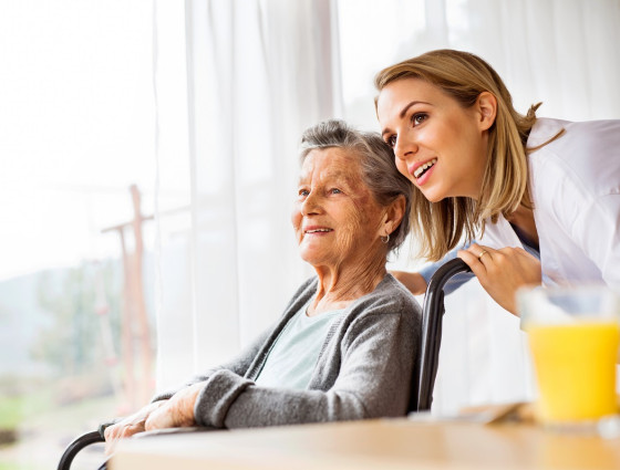 Older person in a chair with a younger person leaning over their shoulder smiling