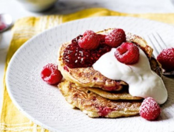Pancakes on plate with yoghurt, jam & raspberries on top