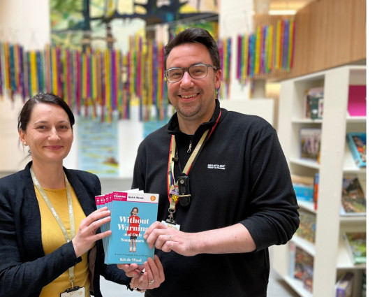 People stand in front of books at the Hive holding a book