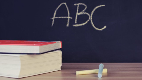 Two books and chalk on a desk in front of a blackboards with ABC written on it.