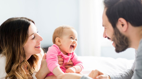 woman holding a smiling baby in pink faces a man 