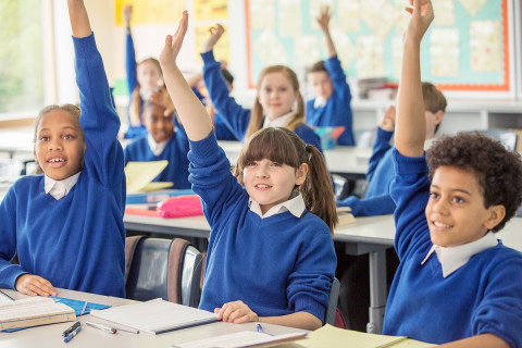 A group of school children in a classroom with their hands up