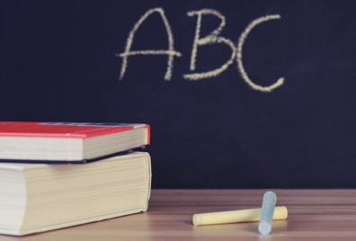Two books and chalk on a desk in front of a blackboards with ABC written on it.