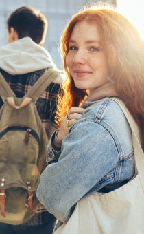 Landscape image of 4 students walking. A girl with long red hair is looking back to the camera