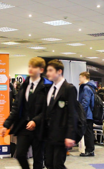 School students attend a carers event at Worcester's Sixways Stadium. they are walking across an exhibition hall with exhibitors in the background.