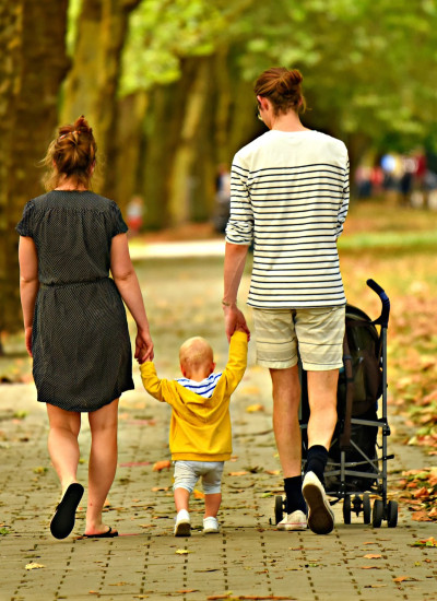 Two women walking away from the camera holding the hands of a small child
